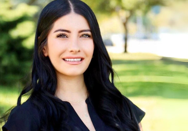 a person with long black hair smiling in front of trees