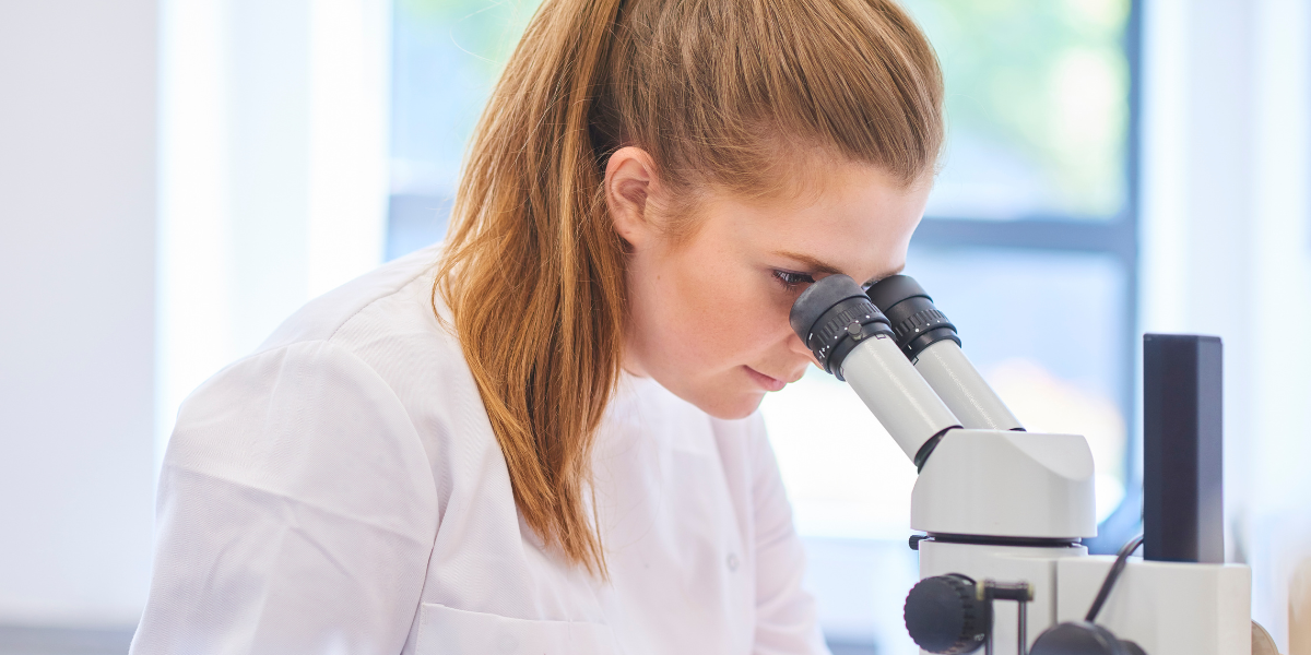 Woman in a lab coat looking through a microscope.