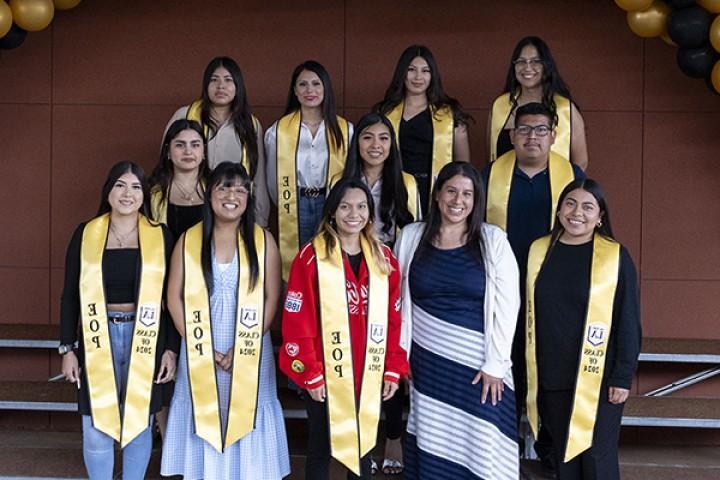 A group of students wearing gold graduation sashes standing in three rows.