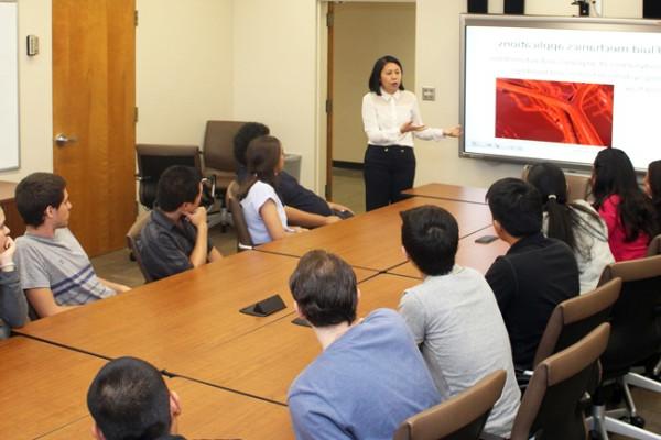 一群足彩外围网站的学生在教室里围绕着会议桌，面对投影仪屏幕，讲师在讲课.